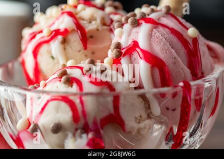 Crème glacée Roma à la fraise, à la banane et à la crème dans un bol en verre avec sauce rouge versée dessus. Banque D'Images