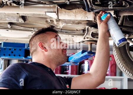 Urla, İzmir, Turquie - juin 2021 : mécanicien automobile utilisant un spray pour les parties inférieures d'une voiture soulevée à la station de réparation automobile. Banque D'Images