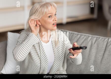 Problèmes d'audition. Femme d'âge mûr regardant la télévision assise sur un canapé Banque D'Images