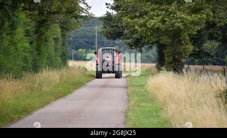Agriculteur conduisant un tracteur rouge a sur la route dans la campagne française. Banque D'Images