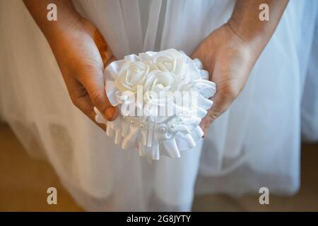 Gros plan des mains d'une jeune demoiselle d'honneur tenant une boîte en satin blanc contenant les anneaux de mariage Banque D'Images