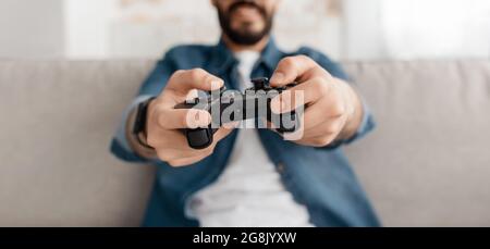 Jeune homme méconnaissable jouant des jeux vidéo avec joystick à la maison, assis sur un canapé, mise au point sélective, rogner, panorama Banque D'Images