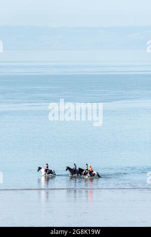 Quatre chevaux sont criés dans la mer à la plage de Barry Island lors d'une matinée ensoleillée d'été. Banque D'Images