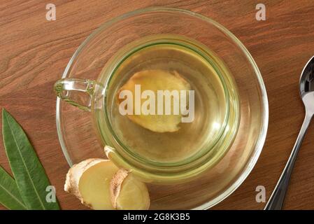 Détail de la tasse avec infusion de gingembre sur une table en bois avec une cuillère et des feuilles. Vue de dessus. Banque D'Images