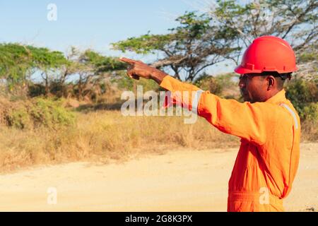Concept d'ingénieur ou de technicien. Mécanicien africain de sexe masculin en uniforme orange et doigt pointé. Banque D'Images