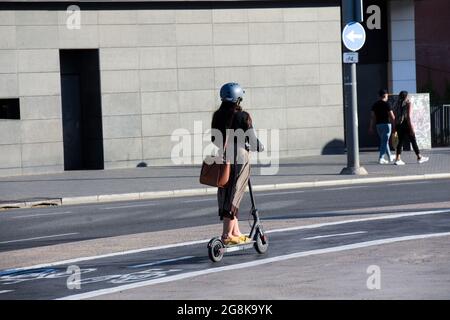 Une jeune femme est à cheval électrique dans une rue d'une ville. Banque D'Images