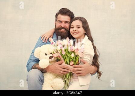 Un cadeau fabuleux pour un enfant. Une famille heureuse fête ses vacances. Le petit enfant et l'homme barbu tiennent des fleurs et du jouet. Petite fille câlin père. Boutique de cadeaux Banque D'Images