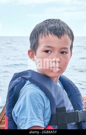 Un garçon asiatique sérieux dans un gilet de sauvetage sur fond de mer et de ciel Banque D'Images