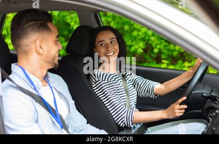 Femme brune excitée assise sur le siège de voiture de conduite, saluant l'instructeur Banque D'Images