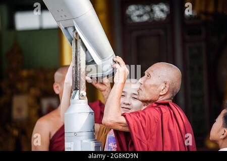 Groupe de moines bouddhistes birmans portant des robes de chambre en marron regardent à travers le télescope à la Pagode Shwedagon, Yangon, Myanmar Banque D'Images