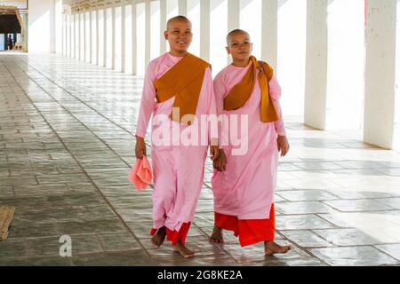 Jeunes nonnes birmanes novices (thilashin) dans leurs tenues roses marchant long couloir au temple Shwezigon Paya, Bagan, Myanmar Banque D'Images