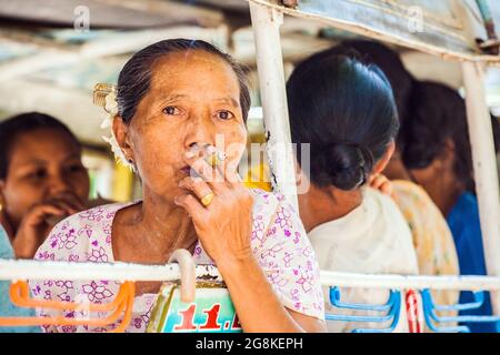 Femme birmane âgée fumant un cigare par la fenêtre du bus local, Monywa, Myanmar Banque D'Images