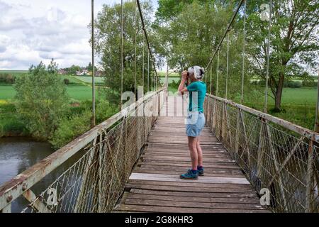 Une femme sur un pont suspendu au-dessus de la rivière Wye, en dessous de Hole in the Wall, Herefordshire, Royaume-Uni. Banque D'Images