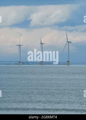 Parc éolien proche de la rive à Redcar, devant un ciel ensoleillé, complexe et nuageux, avec la mer du Nord comme premier plan et le promontoire construit à l'horizon. Banque D'Images