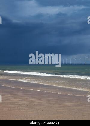 Le parc d'éoliennes près de la rive à Redcar, devant le ciel ensoleillé, sinistre, orageux, avec les vagues ondulantes de la mer du Nord qui se brisent sur la plage en premier plan. Banque D'Images