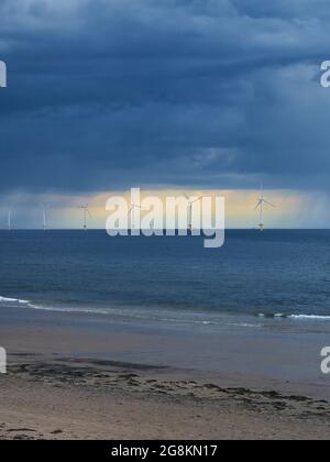 Le parc éolien près de la rive à Redcar Beach, devant la location ensoleillée dans un ciel sinistre et orageux, avec les vagues ondulantes de la mer du Nord en premier plan. Banque D'Images