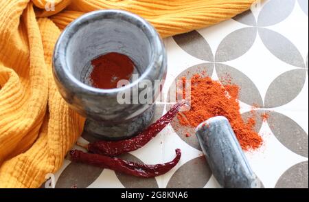 Mortier et pilon en pierre grise, piments et paprika en poudre sur une table. Photo vue du dessus des assaisonnements. Tissu jaune sur fond. Banque D'Images