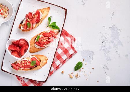 Sandwichs ouverts avec fraises, fromage doux à la menthe et aux noix dans une assiette en céramique sur fond de pierre gris clair. Nourriture estivale et saine, légumes Banque D'Images