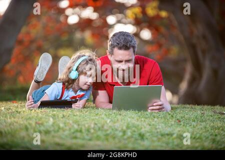 une famille heureuse de papa et de fils utilise un ordinateur portable et des écouteurs dans le parc, week-end familial. Banque D'Images