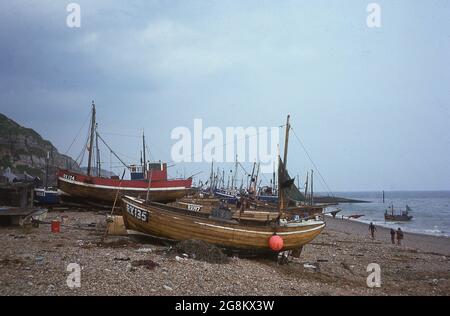 1975, bateaux de pêche traditionnels en bois sur le Stade, une plage de galets dans la vieille ville de Hastings, East.Sussex, Angleterre, Royaume-Uni. Associée à la célèbre bataille de Hastings en 1066, la ville devint plus tard l'un des ports médiévaux de Cinque et, au XIXe siècle, une station balnéaire populaire. L'industrie de la pêche a toujours été importante pour Hastings et la ville possède la plus grande flotte de pêche de plage du Royaume-Uni, basée au Stade, utilisée depuis plus de mille ans, pour le braconnage des bateaux. Banque D'Images