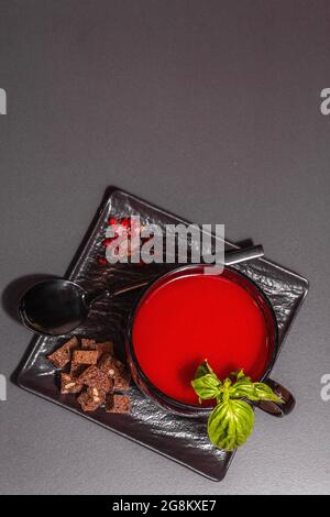 Soupe traditionnelle de tomates dans une tasse. Basilic, croûtons, épices, couverts. Fond en béton de pierre noire, design minimaliste, vue de dessus Banque D'Images