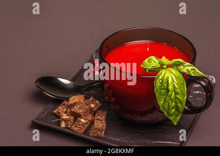 Soupe traditionnelle de tomates dans une tasse. Basilic, croûtons, épices, couverts. Fond en béton de pierre noire, design minimaliste, espace de copie Banque D'Images