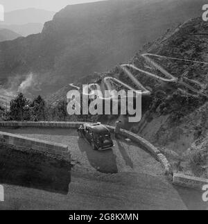 1952, historique, Monaco, un homme à côté de sa voiture garée prenant une photo du paysage environnant et de la route sinueuse de montagne, sur laquelle se déroule le rallye de Monte-Carlo. Le Rallye a débuté en 1911 avec 23 concurrents. Banque D'Images