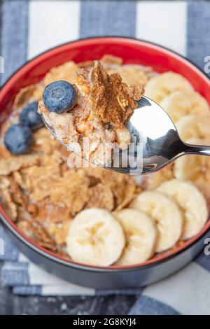 Muesli. Petit déjeuner, alimentation saine et alimentation. Muesli au lait et aux fruits dans une assiette sur un dessus en marbre noir. Main de femme avec une cuillère Banque D'Images