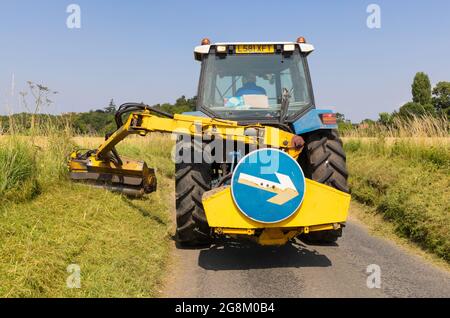 Homme dans un tracteur fauchant des pelouses dans une voie de campagne en été. Beaucoup Hadham, Hertfordshire juillet 2021 Banque D'Images