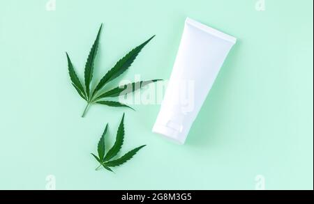 Produit cosmétique de soin de la peau de chanvre dans le tube blanc d'emballage de maquette. Crème ou lotion hydratante au cannabis avec feuilles vue du dessus Banque D'Images