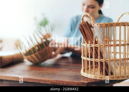 Femme tisse un panier de tubes en papier sur une table en bois. Banque D'Images