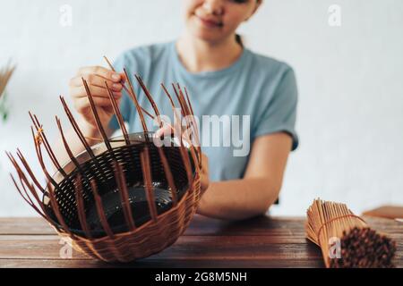 Femme tisse un panier de tubes en papier sur une table en bois. Banque D'Images