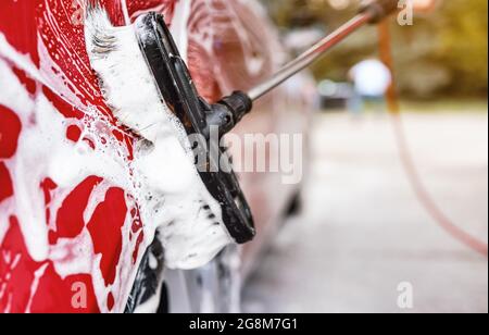 Voiture rouge lavée dans un autoservir carwash , détail sur la brosse laissant des coups sur la porte latérale Banque D'Images