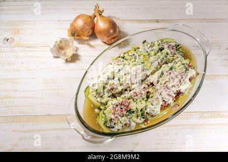 Courgettes ou courgettes farcies à la viande de bœuf hachée, aux oignons et à la crème dans une casserole en verre préparée pour cuire au four sur une languette en bois clair Banque D'Images