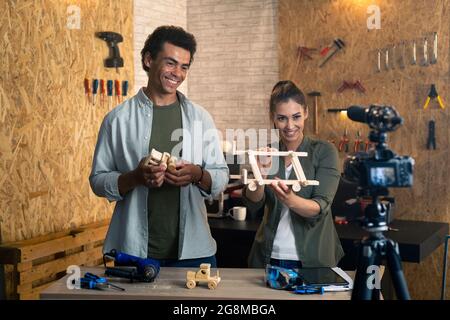 Deux personnes devant l'appareil photo sur le set pour un blog de bricolage dans un atelier de menuiserie. Les menuisiers expliquent le processus de création des jouets en bois Banque D'Images