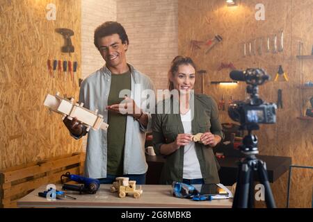 Deux personnes devant l'appareil photo sur le set pour un blog de bricolage dans un atelier de menuiserie. Les menuisiers expliquent le processus de création des jouets en bois Banque D'Images