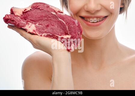 Une jeune femme avec des dents et des bretelles tient la viande de bœuf crue sur la paume de sa main Banque D'Images