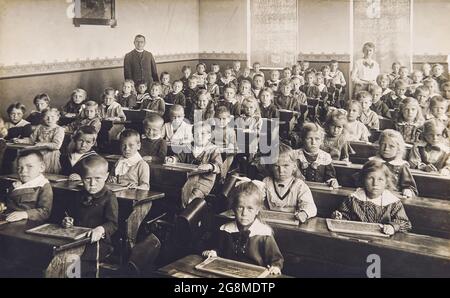 Camarades de classe dans la salle de classe. Enfants et enseignant à l'école. Photo vintage avec grain original, flou et rayures de env. 1910 Banque D'Images