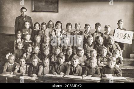 Enfants et enseignant dans la salle de classe. Photo rétro des camarades de classe à l'école. Photo d'époque avec grain de film original à partir de ca 1948 Banque D'Images