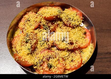 Vue de dessus de la cuisine indienne de rue de la salade de chat de tomates bhelpuri. Tomates fraîches en tranches garnies de chutney au pudina, chutney aux dattes, poivre du sel et Banque D'Images