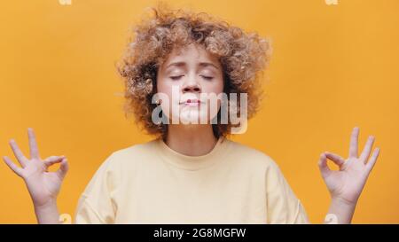 Belle fille tenant les mains dans le geste de yoga. Méditation et yoga. Une fille détendue et sans stress faisant du yoga. Isolé sur fond jaune studio. Une fille concentrée qui se détend l'esprit. Banque D'Images