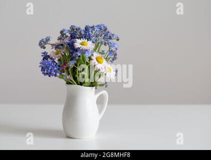 Bouquet de fleurs dans une carafe sur une table blanche. Bouquet de pâquerettes et d'oublis-mes-nots. Composition minimale pour le jour de la Saint-Valentin, le jour de la mère. Copier l'espace. Banque D'Images