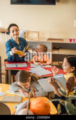 professeur flou pointant avec un stylo à la fille asiatique avec livre pendant la leçon Banque D'Images