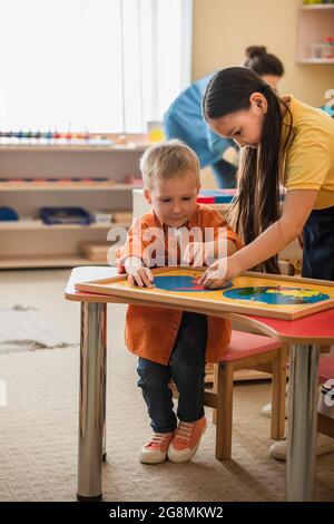 fille asiatique aidant enfant combinant la carte de la terre puzzle près de l'enseignant flou Banque D'Images