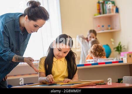 professeur pointant au puzzle près de la fille asiatique à l'école de montessori Banque D'Images