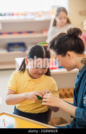 jeune enseignant aidant asiatique fille combinant puzzle près de fille sur fond flou Banque D'Images