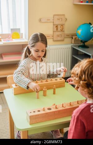 fille jouant au jeu avec un élément en bois près d'un enfant flou à l'école montessori Banque D'Images