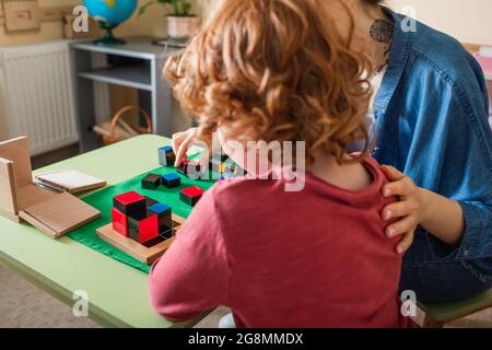 vue arrière du garçon à tête rouge jouant à un jeu éducatif avec un professeur à l'école montessori Banque D'Images