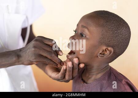 Un jeune garçon noir africain obtient un test de salive PCR par un médecin africain dans un village rural à l'extérieur de Bamako, Mali. Banque D'Images