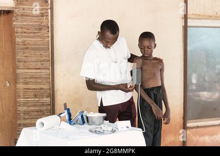 Dans cette photo, un jeune professionnel de la santé prend les valeurs de pression artérielle d'un petit garçon noir lors d'un contrôle de routine dans un milieu hospitalier rural en AF Banque D'Images